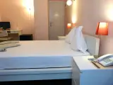 Comfort Double room bed with pillows, red lamp and telephone on nightstand, desk with TV beyond